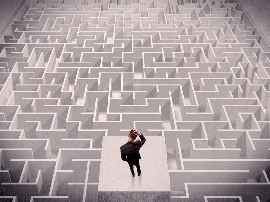 man standing on podium scratching his head as he looks at a maze in front of him