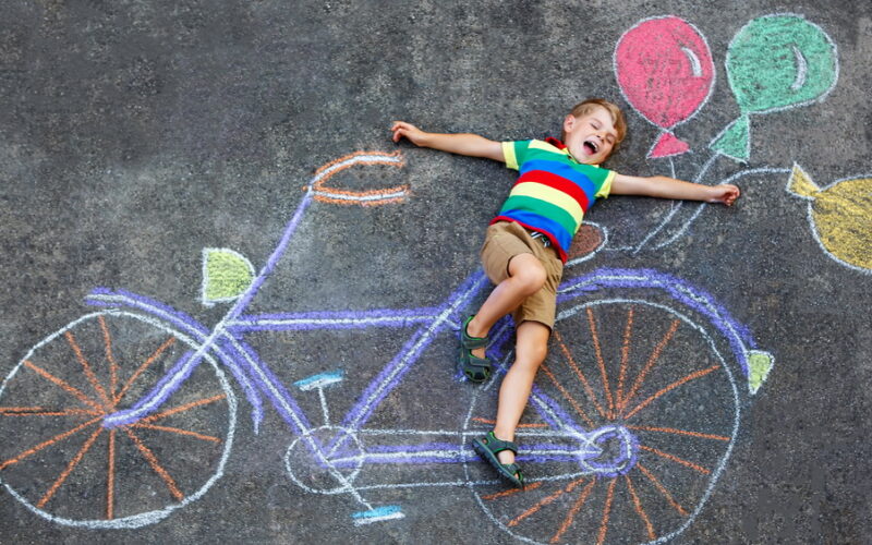 child laying on a chalk drawing of a bicycle with colorful balloons attached