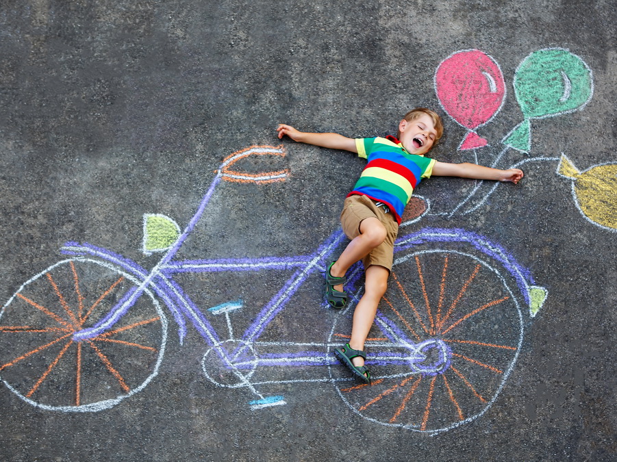 child laying on a chalk drawing of a bicycle with colorful balloons attached