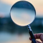 magnifying glass held up to a blurry horizon line at twilight